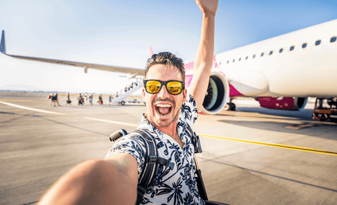 Man taking a selfie in front of an airplane with a clear sky